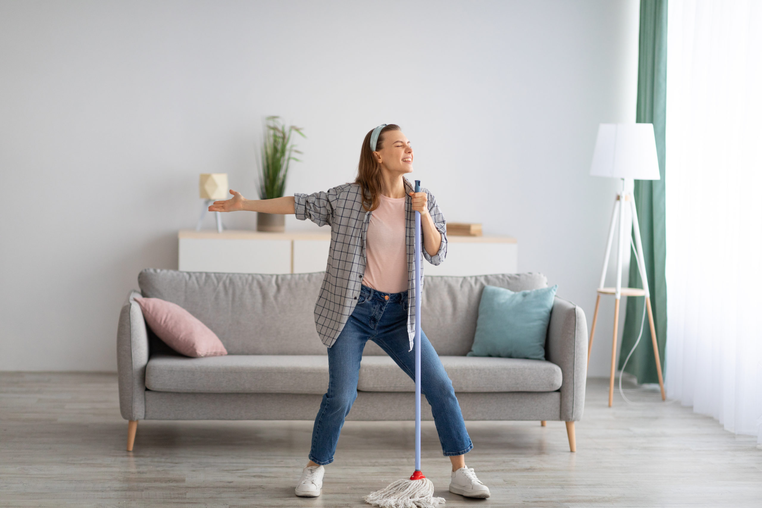 Woman using broom as microphone while cleaning her living room.